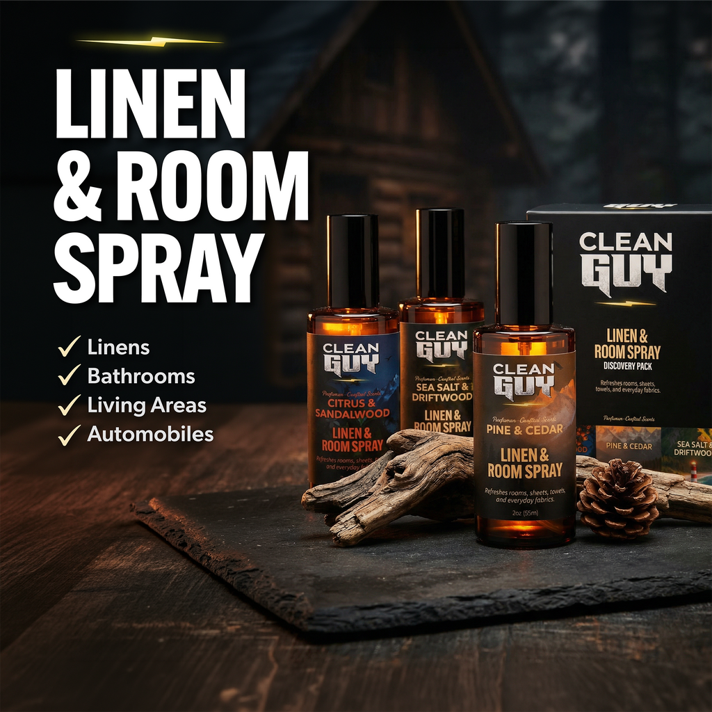 Three bottles of Clean Guy linen and room spray on a dark surface with packaging and decorative elements.